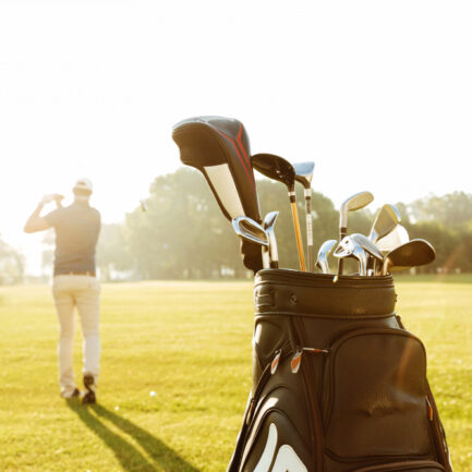 A golf bag filled with golf clubs on a golf club, with a man swinging his club in the background