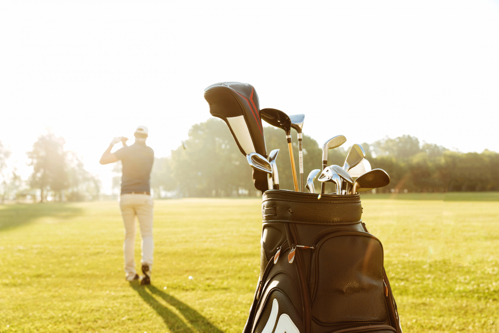 A golf bag filled with golf clubs on a golf club, with a man swinging his club in the background